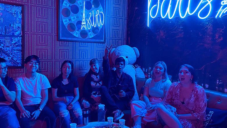 UQ Karaoke Club sit in a blue-lit room with neon lights