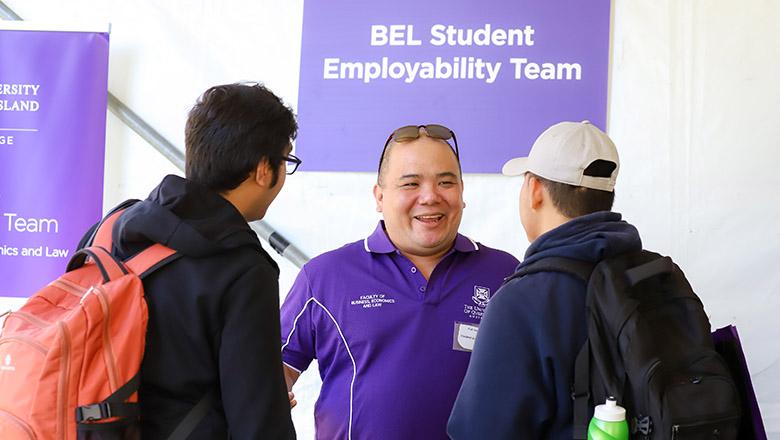 Two students talk to a UQ staff member under a sign that says 'BEL student employability team'