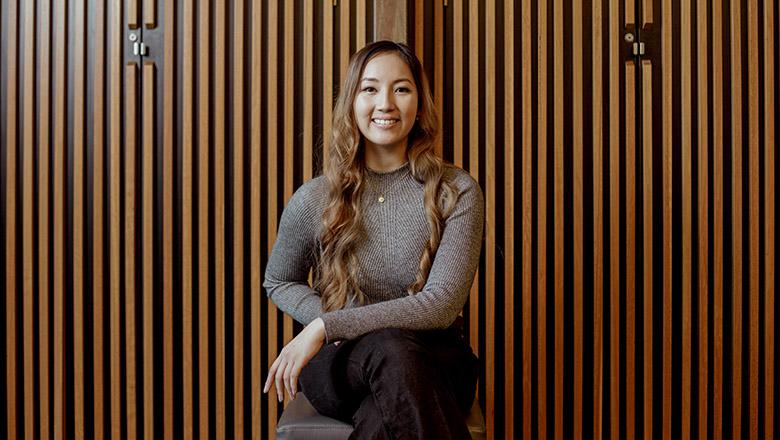 UQ Communication student Dianne Mai sits smiling in front of a wooden panelled wall