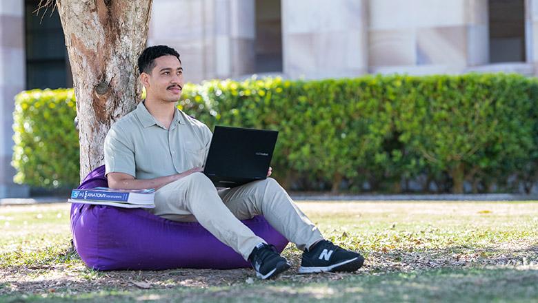 Nathan Sagigi sits on a beanbag with his laptop in the Great Court at UQ