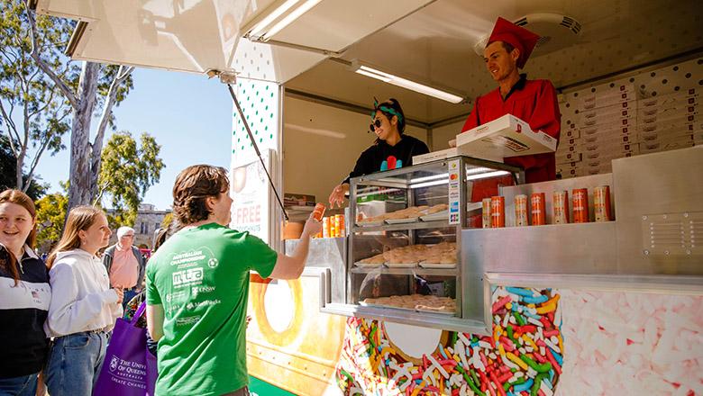 Workers at a Krispy Kreme food truck hand out boxes of donuts to UQ students