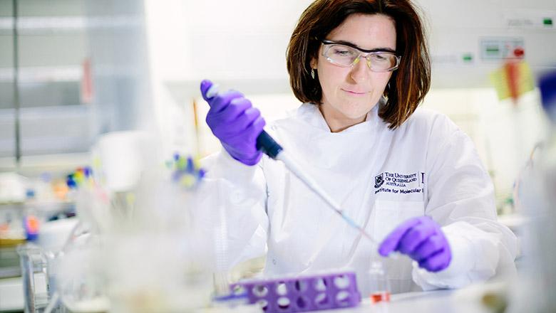Biotechnology researcher Avril Robertson wears a lab coat, safety glasses and plastic gloves and inspects a large needle-like instrument which she is holding