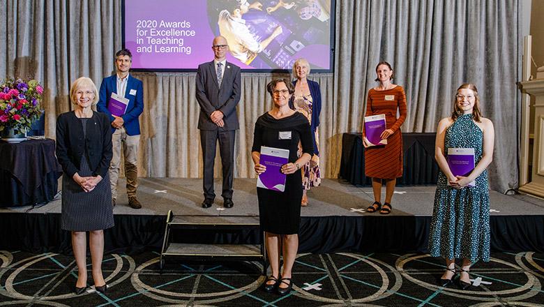 Several teachers including Leigh Sperka stand on a stage holding certificates while physically distancing at the 2020 Teaching Excellence Awards