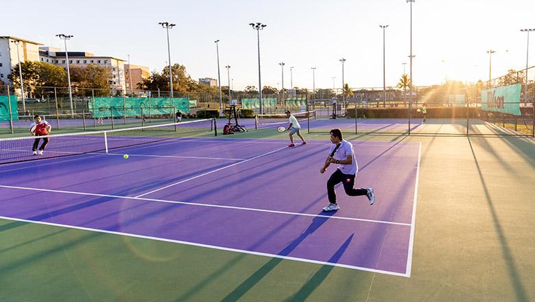 People playing doubles on a purple UQ tennis court with the sun setting in the background
