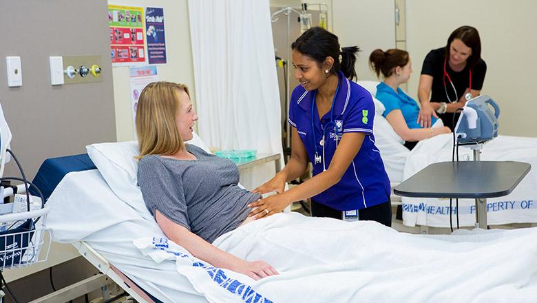 A student midwife tends to a pregnant woman in a hospital bed
