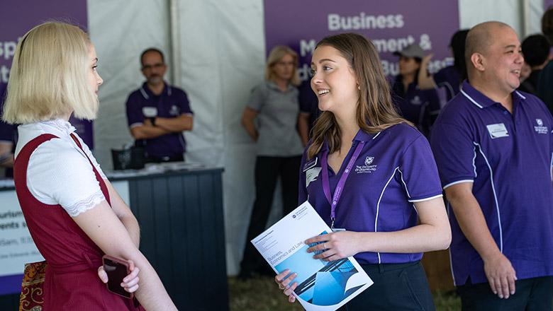 A student ambassador in a purple UQ polo talks to a high school student about studying business at UQ