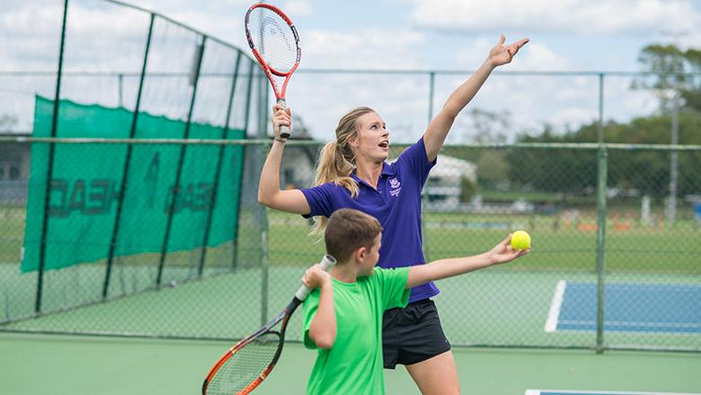 A woman teaches a boy how to serve on a tennis court