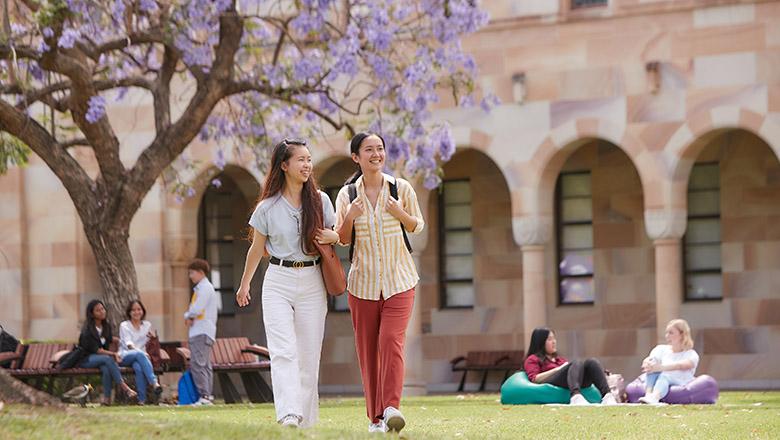 Female students walk through UQ's Great Court with sandstone cloisters in background