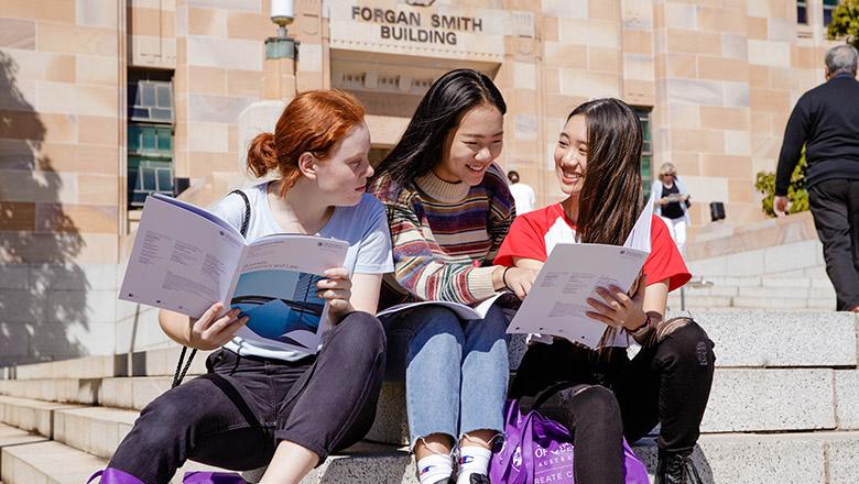 Three young women browse brochures outside UQ's sandstone buildings on Open Day