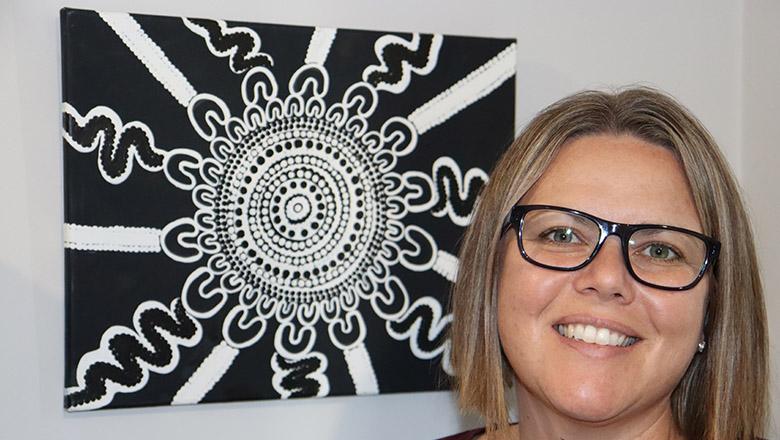 Marnee Shay stands in front of Aboriginal artwork by Aunty Denis Proud