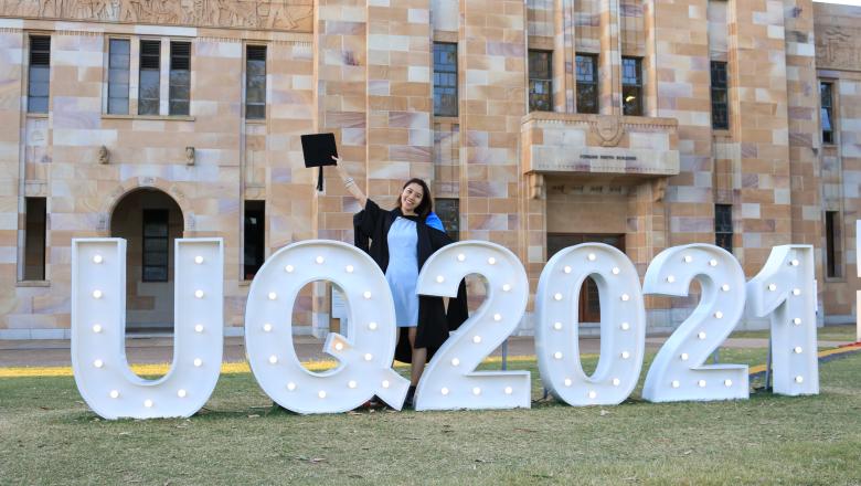 Fiona standing in her graduation gown in front of the UQ 2021