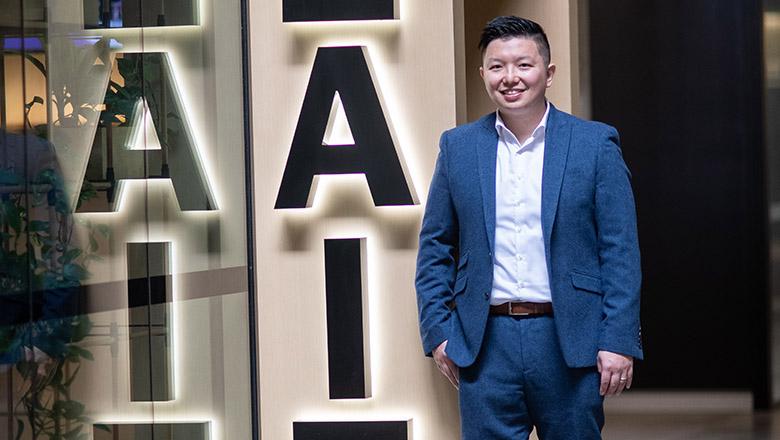 Professor Ryan Ko stands in from of a sign with a lit up 'A' and 'I' letters