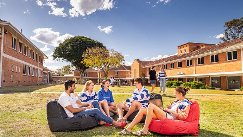 Students sitting on bean bags in the sunshine, on the grounds of UQ's Emmanuel College, talking and laughing