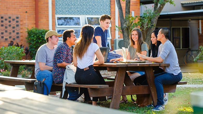 Students sit around a picnic table in an outdoor green space