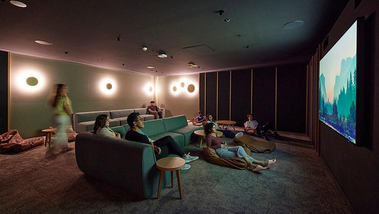 Students sitting on lounges and bean bags watching a movie on a big screen in a home cinema at Kev Carmody House