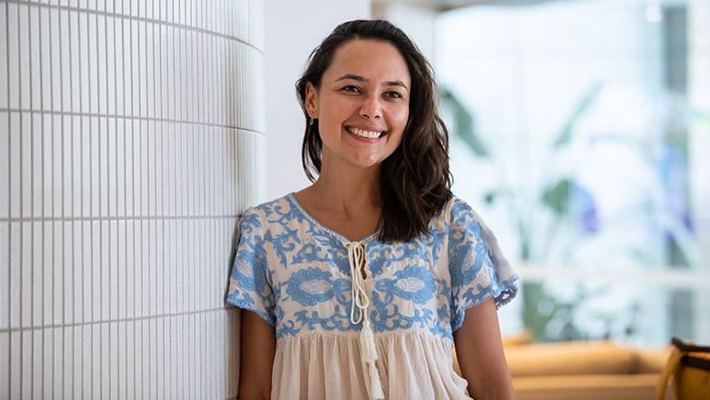 Barbara Azevedo de Oliveira stands smiling at UQ's Student Central, leaning against a white tile wall