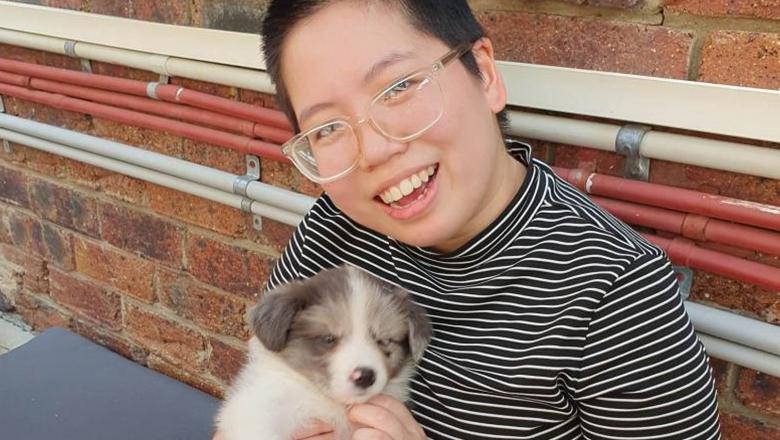 Li Xuan Tan sits holding a puppy and smiling