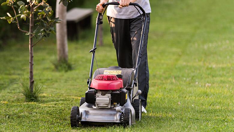 Image of a person from the waist down pushing a lawn mower over green grass