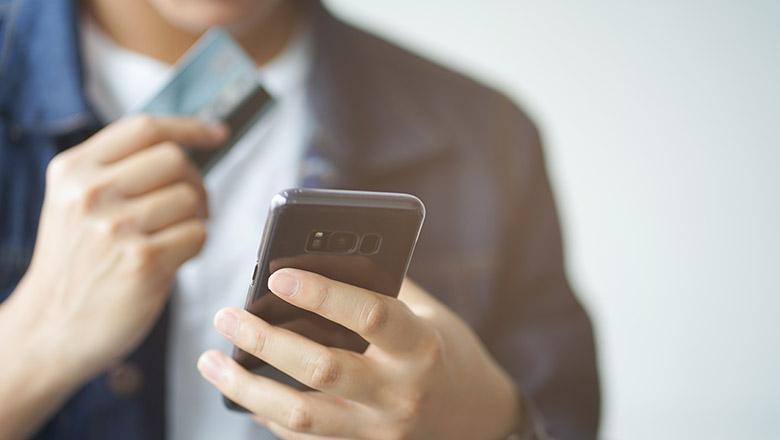 Closeup of a person holding a smartphone in one hand, and a bank card in the other