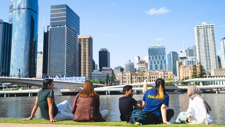 5 students sitting on the grass next to the Brisbane river