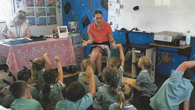 UQ Student Isabelle Taylor sits on a chair talking to a classroom of junior school students