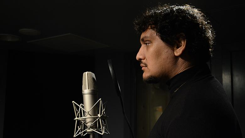Jamaine stands in front of a microphone in a recording studio