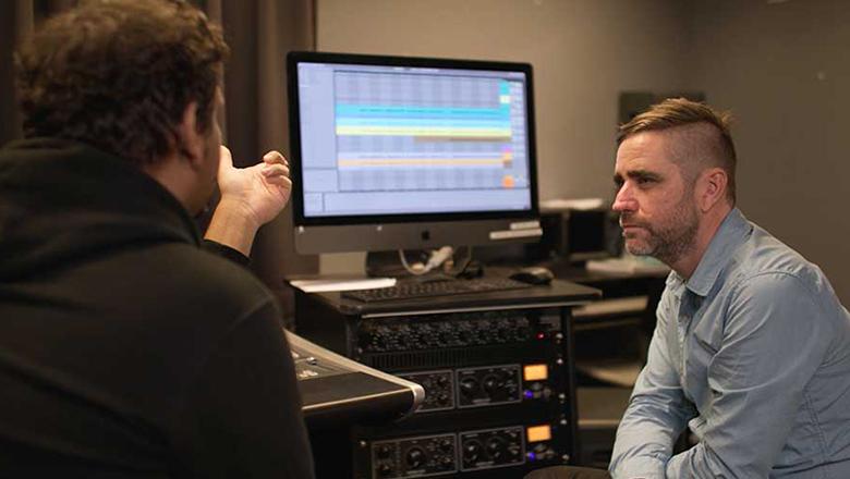 Jamaine and Dr Chris Perren sit in the recording studio with a computer screen and sound desk