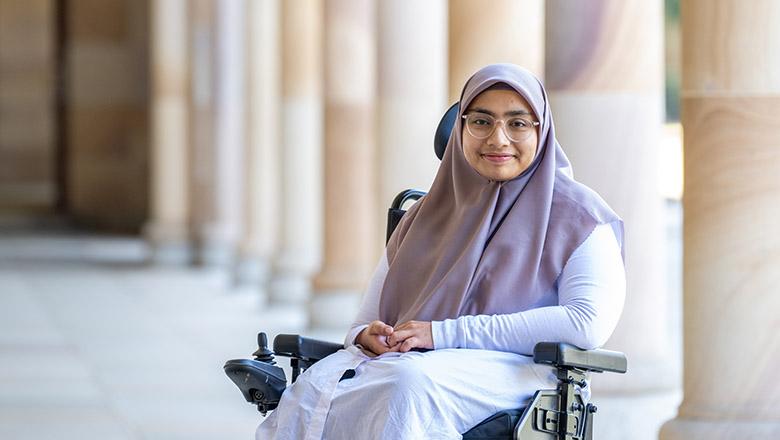 Aisyah Ardani, UQ Master of Educational Studies student sits in a wheelchair with sandstone pillars in the background