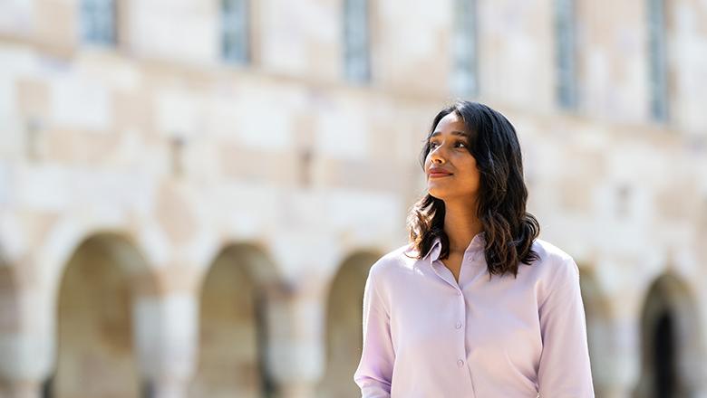 Nisha Gupta, UQ Master of Counselling student stands in St Lucia campus' Great Court with sandstone cloisters in background
