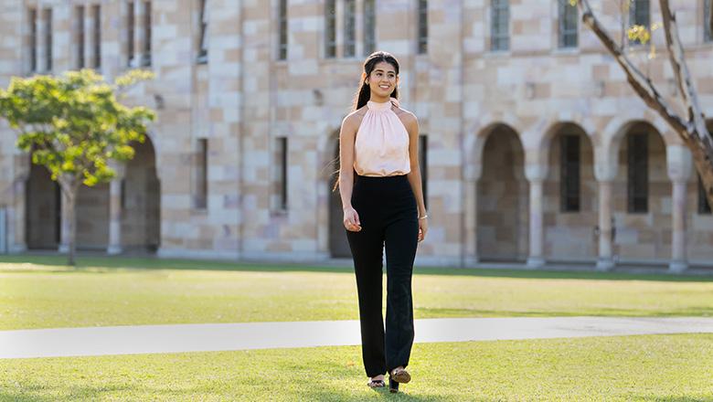 Ramneet Ubbi walks across UQ St Lucia's Great Court with sandstone cloisters in the background