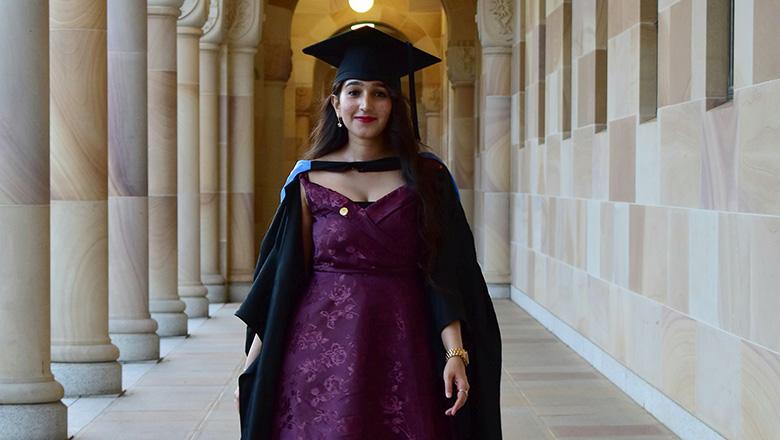 Shrika Charbhe stands in UQ St Lucia's sandstone cloisters in a graduation cap and gown