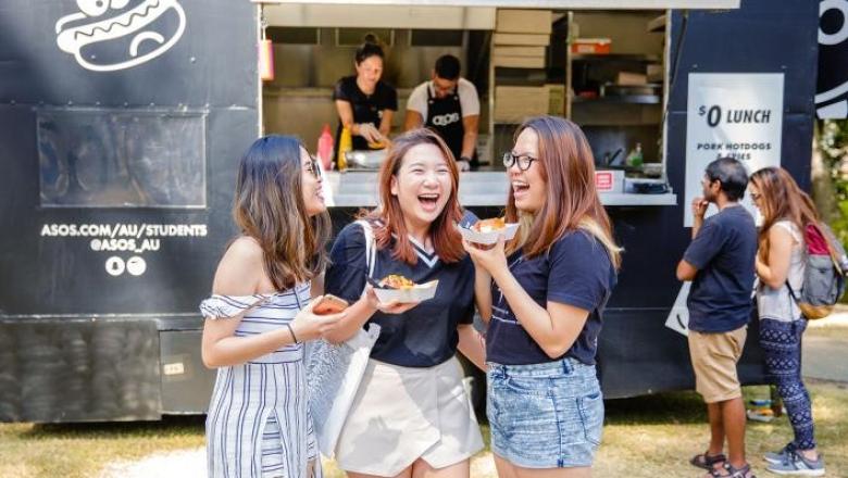 3 students laughing in front of a food truck