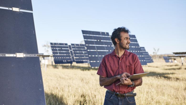 A UQ PhD candidate stands in a field of solar panels with a clipboard