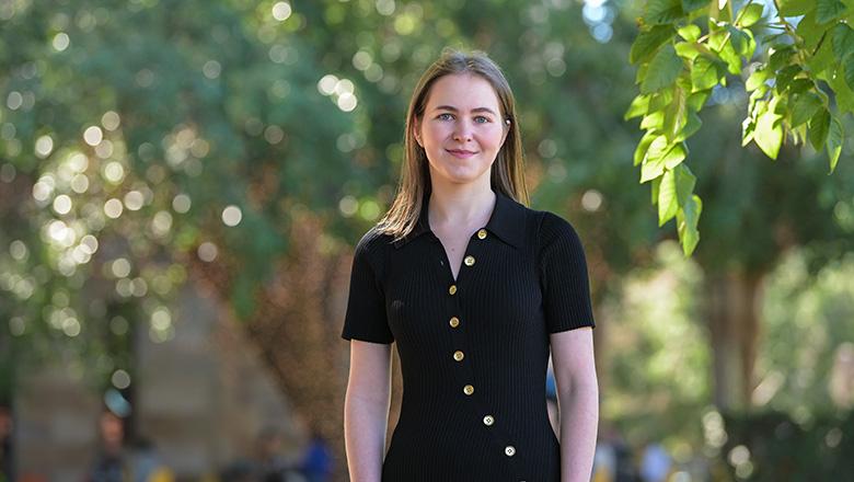 Sophia Dow stands in the Great Court surrounded by trees at UQ St Lucia campus