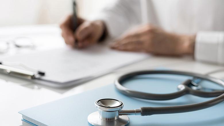 Stethoscope next to someone writing in a medical chart