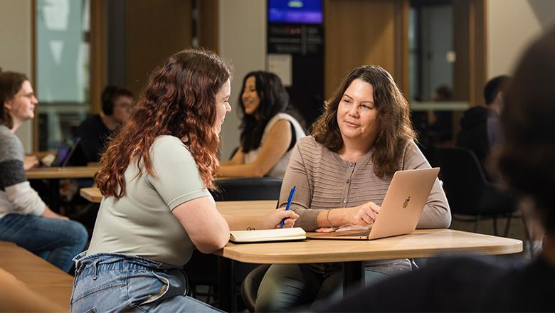 A UQ student sits at a desk in discussion with a mentor