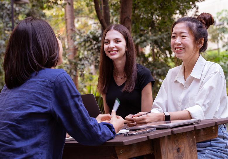 A group of UQ students sitting outside having a conversation, smiling.