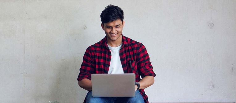 A young student in the centre of the frame happily looks at their laptop