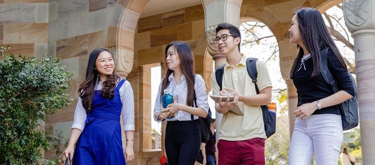 Four students walking through sandstone arches at the St Lucia campus.