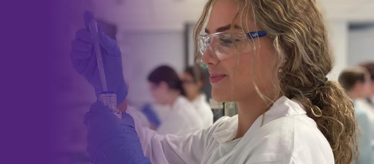 Female student in research lab wearing science glasses and lab coat. 