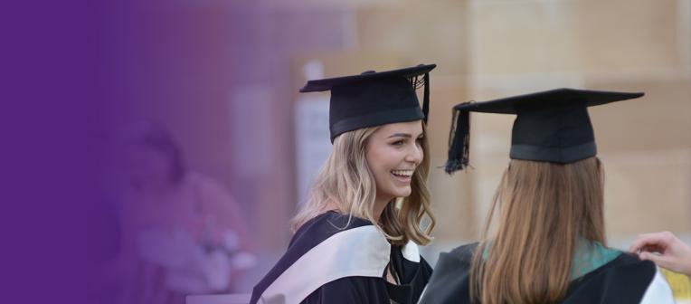 Two young women wear graduation gowns and mortarboards 