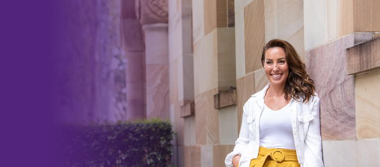 Natalie Craig stands smiling in front of UQ's sandstone buildings