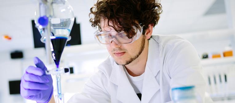 UQ chemistry student looks at blue liquid in a beaker