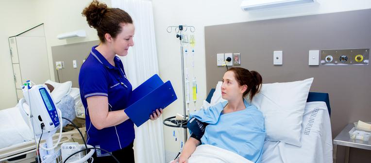 A UQ nursing student talks to a patient in a hospital bed