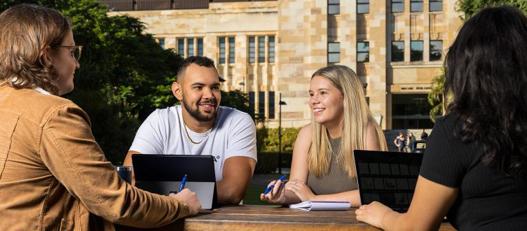 UQ students studying at a picnic table in front of sandstone buildings