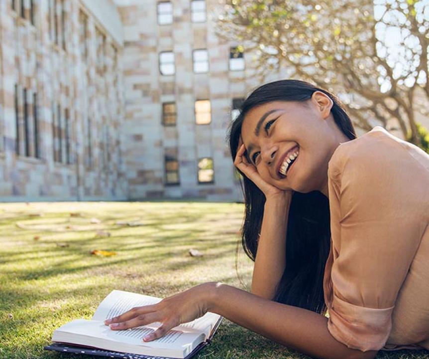 A student reading on the grass outside the Forgan Smith building at St Lucia campus.