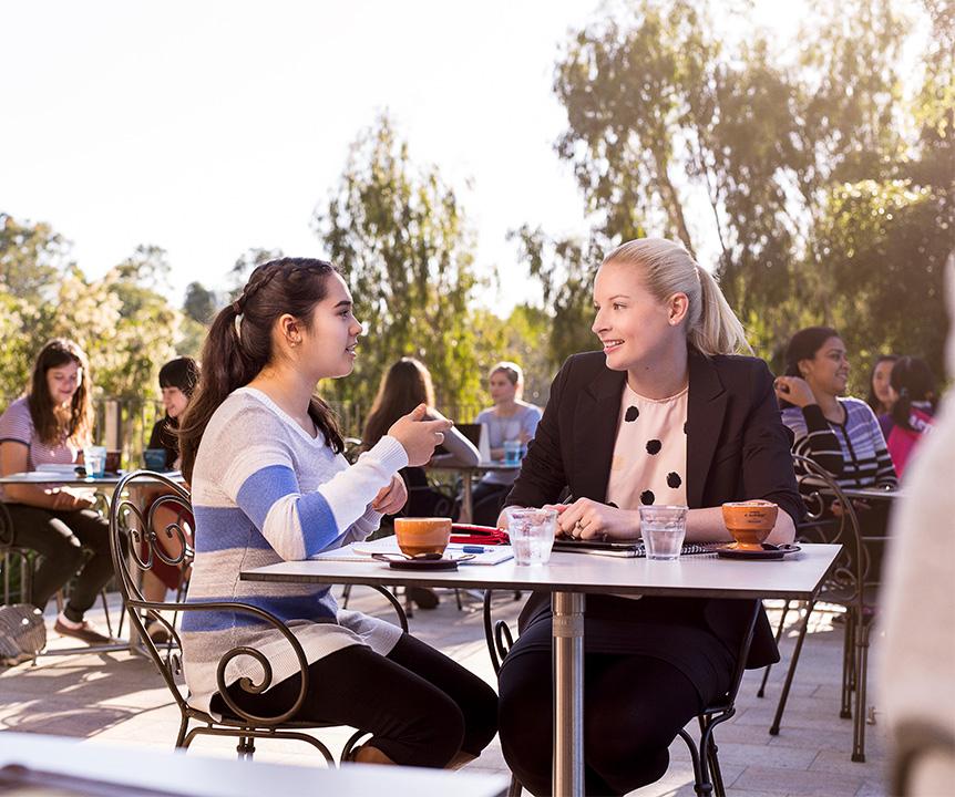 Students chatting over coffee at a café with trees in the background.