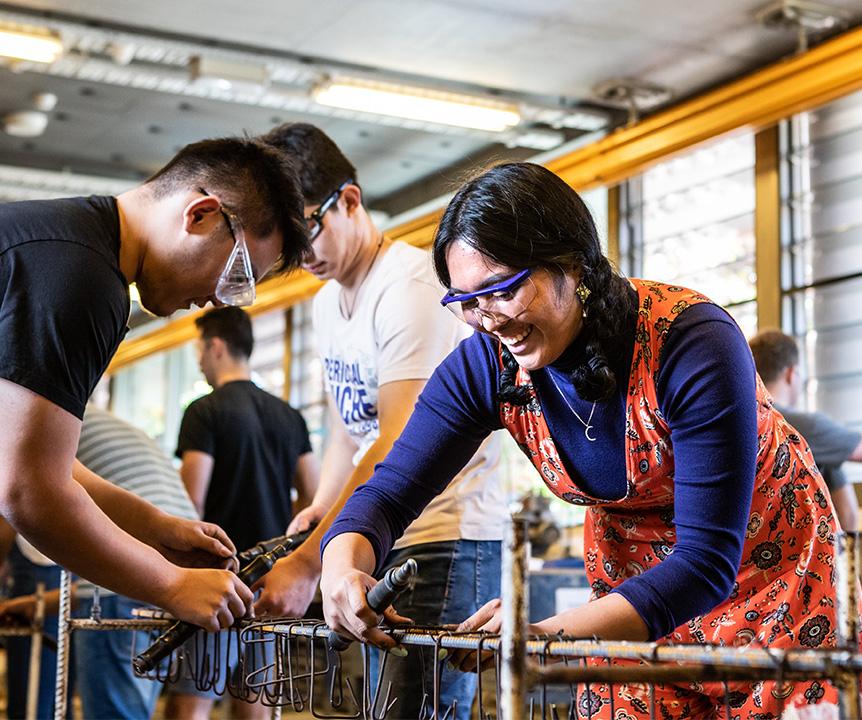 Three students wearing protective glasses and working on a project in a workshop.