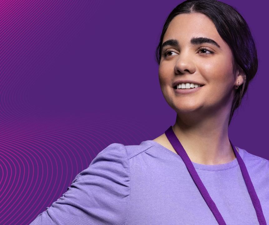 Women in a purple shirt and purple lanyard smiles in front of a purple background. 