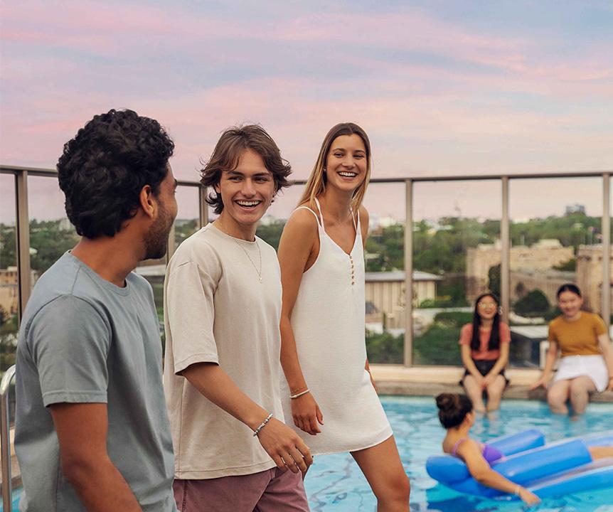 Three students walk past a rooftop pool at sunset.